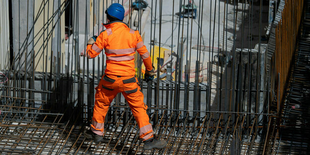 Bauarbeiter in oranger Schutzkleidung verlegt Stahlmatten