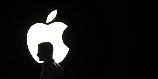 Der Kopf eines Mannes wird als Silhouette vor dem Apple-Logo sichtbar Der Kopf eines Mannes wird als Silhouette vor dem Apple-Logo sichtbar