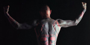 Ein tätowierter Mann zeigt seinen Rücken und seine Muskeln.