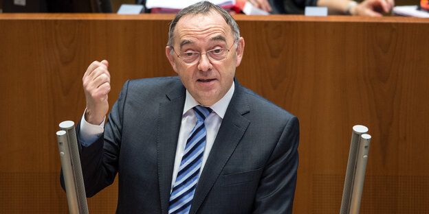 Ein älterer Mann im Anzug und mit Brlle steht an einem Pult und redet. Er hebt die angewinkelten linken Arm und ballt die Faust Ein älterer Mann im Anzug und mit Brlle steht an einem Pult und redet. Er hebt die angewinkelten linken Arm und ballt die Faust