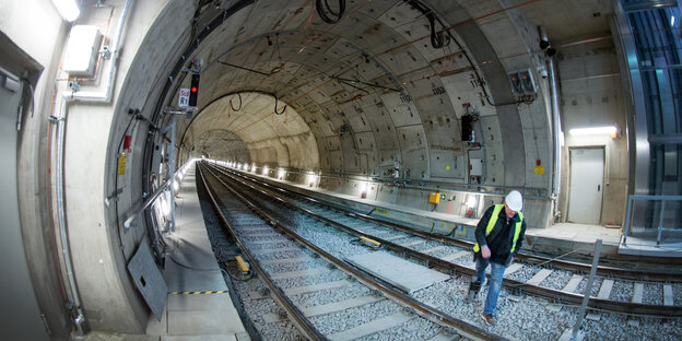 Ein Mann mit Schutzhelm geht durch einen hellen und nicht befahrenen U-Bahn-Tunnel Ein Mann mit Schutzhelm geht durch einen hellen und nicht befahrenen U-Bahn-Tunnel