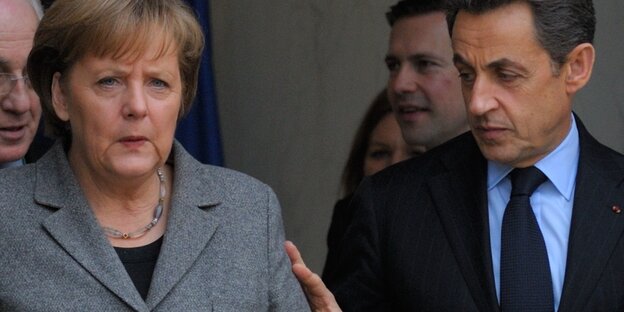 Sarkozy legt seine Hand an Merkels Arm. Beide schauen grimmig. Sarkozy legt seine Hand an Merkels Arm. Beide schauen grimmig.
