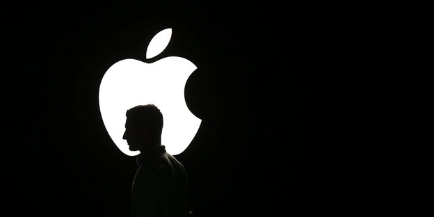 Ein weißes Apple Logo, vor dem eine Kopf zu sehen ist, vor schwarzem Hintergrund. Ein weißes Apple Logo, vor dem eine Kopf zu sehen ist, vor schwarzem Hintergrund.