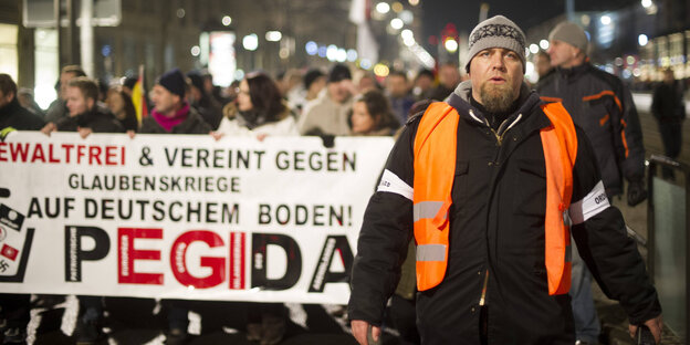 Ein korpulenter Mann läuft vor einer Pegida-Demo. Ein korpulenter Mann läuft vor einer Pegida-Demo.
