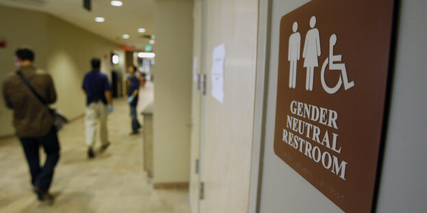 Ein Schild weist in englischer Sprache auf genderneutrale Toiletten hin. Ein Schild weist in englischer Sprache auf genderneutrale Toiletten hin.