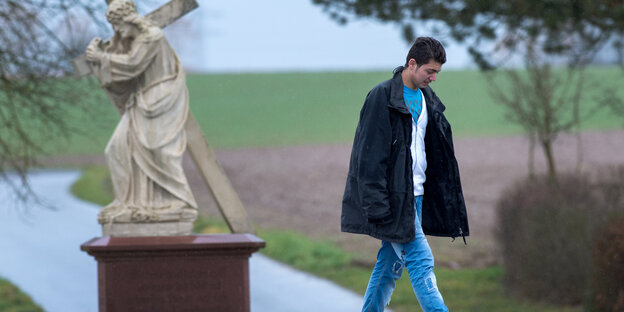 Neben einer Statue, die Jesus ein Kreuz tragend zeigt, läuft ein junger Mann Neben einer Statue, die Jesus ein Kreuz tragend zeigt, läuft ein junger Mann