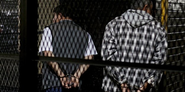 zwei Männer stehen mit gefesselten Händen hinter einem Gitter zwei Männer stehen mit gefesselten Händen hinter einem Gitter