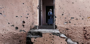 Eine Frau in einem Eingang, Einschusslöcher in einer Wand