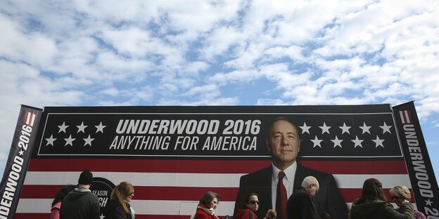 Menschen vor einem riesigen Plakat mit einem Mann, US-Fahne und der Aufschrift "Underwood 2016 - Anything for America"