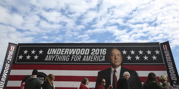 Menschen vor einem riesigen Plakat mit einem Mann, US-Fahne und der Aufschrift "Underwood 2016 - Anything for America" Menschen vor einem riesigen Plakat mit einem Mann, US-Fahne und der Aufschrift "Underwood 2016 - Anything for America"