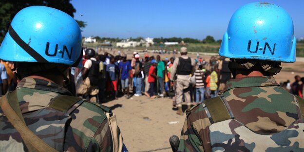 Zwei Blauhelme in Ausrüstung mit Menschen im Hintergrund Zwei Blauhelme in Ausrüstung mit Menschen im Hintergrund