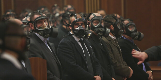 Männer in Anzügen und aufgesetzten Tränengasmasken sitzen in einer Reihe Männer in Anzügen und aufgesetzten Tränengasmasken sitzen in einer Reihe