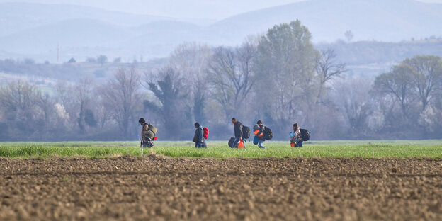 Flüchtlinge mit Taschen und Rucksack gehen durch eine Wiesen- und Ackerlandschaft. Straße rn Flüchtlinge mit Taschen und Rucksack gehen durch eine Wiesen- und Ackerlandschaft. Straße rn