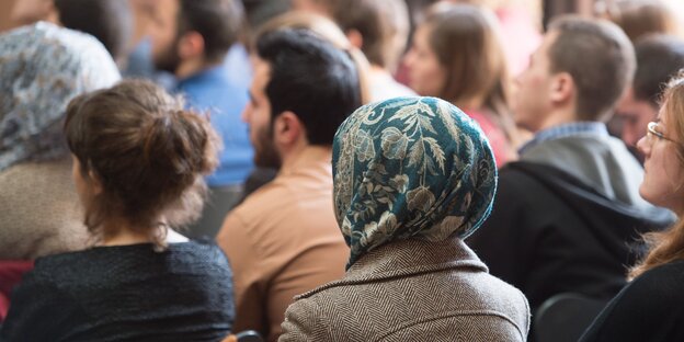 Frauen mit und ohne Kopftuch sitzen nebeneinander. Man sieht sie von hinten. Frauen mit und ohne Kopftuch sitzen nebeneinander. Man sieht sie von hinten.