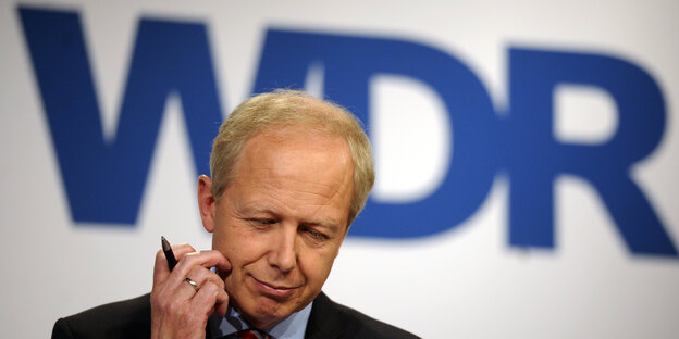 Ein Mann sitzt vor einem WDR-Logo. Ein Mann sitzt vor einem WDR-Logo.