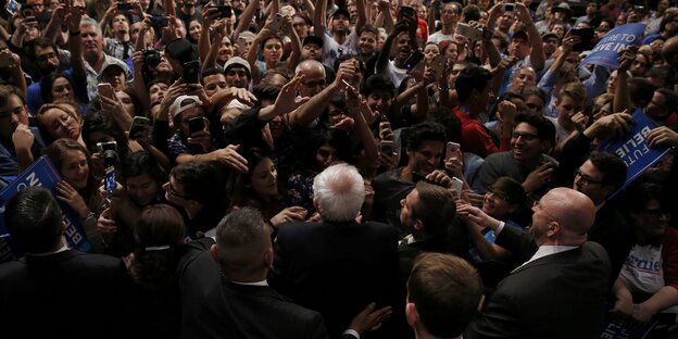 Eine Aufnahme von oben auf Bernie Sanders umringt von Menschen, die ihn fotografieren Eine Aufnahme von oben auf Bernie Sanders umringt von Menschen, die ihn fotografieren