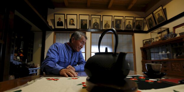 Ein älterer Mann erzählt, im Vordergrund eine Teekanne, im Hintergrund Familienportraits Ein älterer Mann erzählt, im Vordergrund eine Teekanne, im Hintergrund Familienportraits