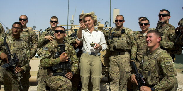 eine Frau in weißer Bluse zeigt inmitten von Soldaten in Uniform auf etwas vor ihr eine Frau in weißer Bluse zeigt inmitten von Soldaten in Uniform auf etwas vor ihr