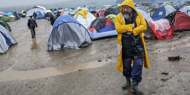 Ein Mann im Regencape vor Zelten Ein Mann im Regencape vor Zelten