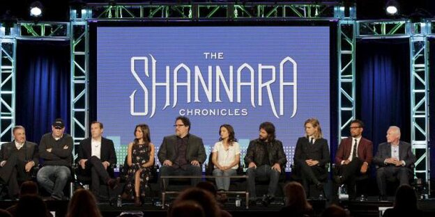 Menschen sitzen in einer Reihe vor einem Bildschirm mit der Aufschrift: „The Shannara Chronicles“. Menschen sitzen in einer Reihe vor einem Bildschirm mit der Aufschrift: „The Shannara Chronicles“.