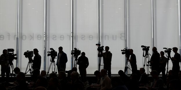 Journalisten mit Kameras stehen vor einer grau-weiße Wand. Journalisten mit Kameras stehen vor einer grau-weiße Wand.