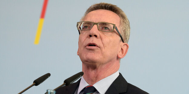 De Maizière, mit Anzug, Krawatte und Brille, spricht ins Mikrophon