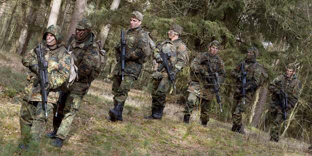 Soldaten in Tarnuniformen und mit Gewehren gehen durch den Wald. Soldaten in Tarnuniformen und mit Gewehren gehen durch den Wald.