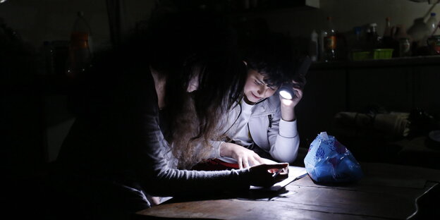 zwei Menschen sitzen mit Taschenlampe am Tisch und lesen etwas, sonst ist es dunkel zwei Menschen sitzen mit Taschenlampe am Tisch und lesen etwas, sonst ist es dunkel