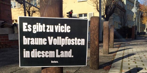 Holzpfosten hintereinander, an einem ein Schild mit der Aufschrift: "Es gibt zu viele braune Vollpfosten in diesem Land." Holzpfosten hintereinander, an einem ein Schild mit der Aufschrift: "Es gibt zu viele braune Vollpfosten in diesem Land."