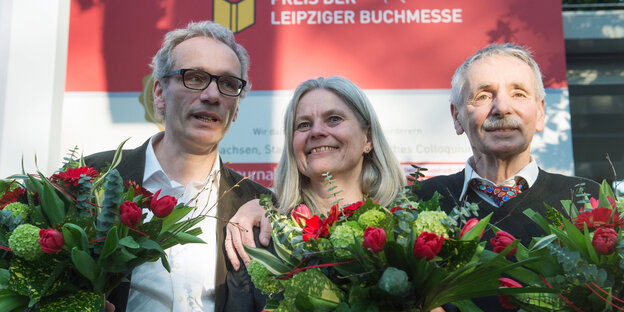 Mann mit Brille, Frau, Mann nebeneinander, lächelnd, mit Blumensträußen Mann mit Brille, Frau, Mann nebeneinander, lächelnd, mit Blumensträußen