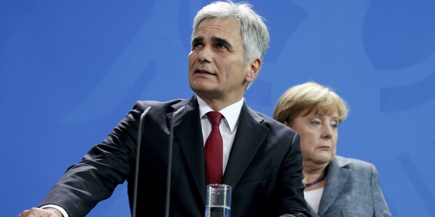 Werner Faymann steht am Rednerpult, dahinter Angela Merkel.