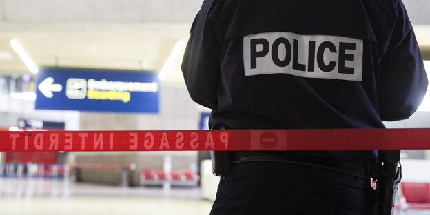Ein französischer Polizist mit der Aufschrift "Police" auf der Rückseite seiner Jacke vor einem Absperrband Ein französischer Polizist mit der Aufschrift "Police" auf der Rückseite seiner Jacke vor einem Absperrband