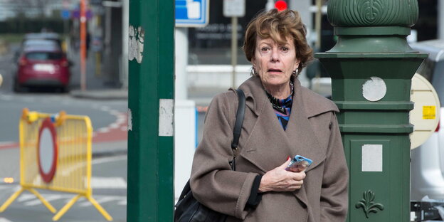 Neelie Kroes steht mit ihrem Smartphone auf einer Straße in Brüssel und schaut erschrocken Neelie Kroes steht mit ihrem Smartphone auf einer Straße in Brüssel und schaut erschrocken