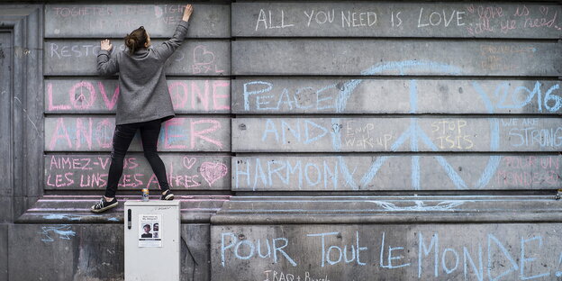 Eine junge Frau malt mit Kreide an eine Wand, auf die unter anderem ein großes Peace-Zeichen gemalt wurde Eine junge Frau malt mit Kreide an eine Wand, auf die unter anderem ein großes Peace-Zeichen gemalt wurde