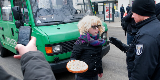 Frau mit Torte wird von Polizist am Weitergehen gehindert