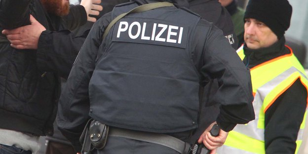der Rücken eines Polizisten, auf seiner Jacke steht „Polizei“