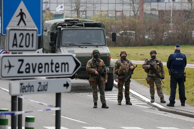 Schwer bewaffnete Soldaten riegeln eine Straße ab. Im Vordergrund: Hinweisschild zum Flughafen. Im Hintergrund: Militärlaster Schwer bewaffnete Soldaten riegeln eine Straße ab. Im Vordergrund: Hinweisschild zum Flughafen. Im Hintergrund: Militärlaster