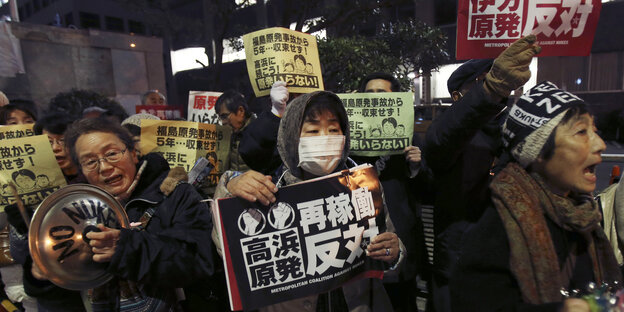 Demonstranten mit Mundschutz halten Schilder mit japanischen Schriftzeichen in die Höhe Demonstranten mit Mundschutz halten Schilder mit japanischen Schriftzeichen in die Höhe