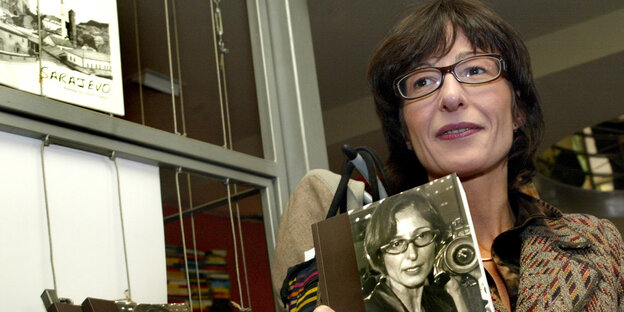Eine Frau mit dunklen Haaren und Brille hält ein Buch Eine Frau mit dunklen Haaren und Brille hält ein Buch