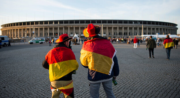Zwei Männer, gehüllt in Deutschland-Fahnen, vor einem Stadion Zwei Männer, gehüllt in Deutschland-Fahnen, vor einem Stadion