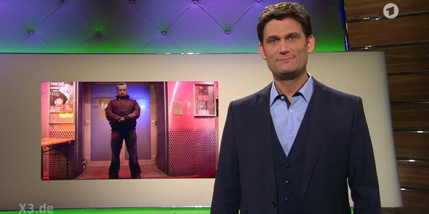 Mann in Anzug, es ist NDR-Moderator Christian Ehring, vor einem Schaubild mit einem Mann drauf Mann in Anzug, es ist NDR-Moderator Christian Ehring, vor einem Schaubild mit einem Mann drauf
