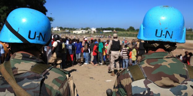 Zwei Soldaten mit blauen UN Helmen, eine Menschenmenge im Hintergrund