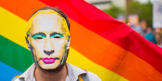 Mann mit geschminkter Putinmaske vor einer Regenbogenfahne Mann mit geschminkter Putinmaske vor einer Regenbogenfahne