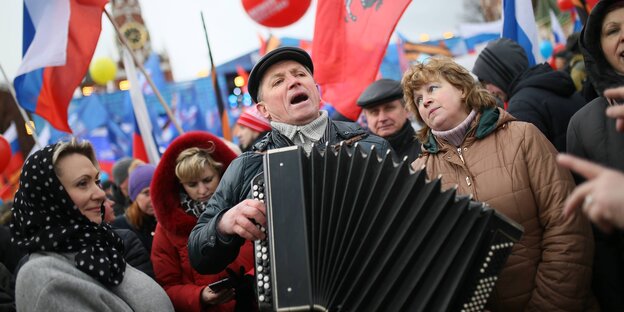 Ein Mann spielt Akkordeon auf dem Roten Platz in Moskau, drumherum stehen ihm zuhörende Menschen Ein Mann spielt Akkordeon auf dem Roten Platz in Moskau, drumherum stehen ihm zuhörende Menschen