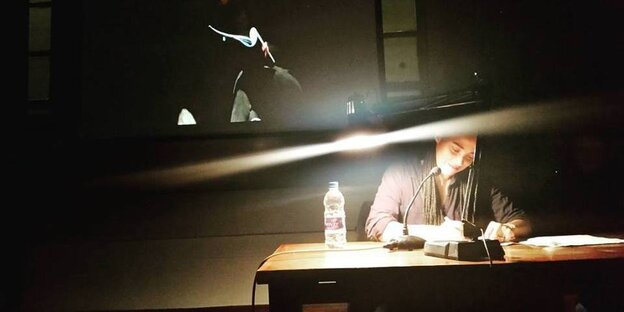 Eine Frau sitzt an einem Tisch an die Wand hinter ihr wird ein Bild projiziert Eine Frau sitzt an einem Tisch an die Wand hinter ihr wird ein Bild projiziert