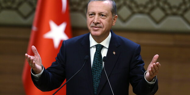 Ein Mann steht vor der türkischen Flagge an einem Rednerpult und gestikuliert mit beiden Händen. Es ist der türkische Präsident Erdogan Ein Mann steht vor der türkischen Flagge an einem Rednerpult und gestikuliert mit beiden Händen. Es ist der türkische Präsident Erdogan