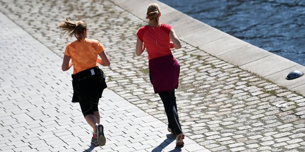 Zwei Frauen von hinten, die an der Spree entlang joggen Zwei Frauen von hinten, die an der Spree entlang joggen
