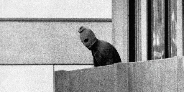 Ein Mann, der eine Sturmhaube trägt, beugt sich über einen Balkon Ein Mann, der eine Sturmhaube trägt, beugt sich über einen Balkon
