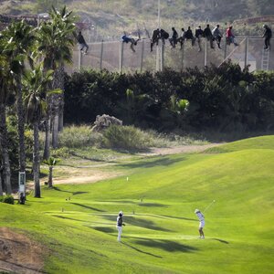 Flüchtlinge Kletern über den Zaun in Melilla, unten spielen Menschen auf einem Golfplatz Flüchtlinge Kletern über den Zaun in Melilla, unten spielen Menschen auf einem Golfplatz