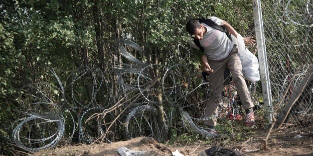 EIn Flüchtlinge klettert im Herst 2015 durch ein Loch in Zaun von Serbien nach Ungarn EIn Flüchtlinge klettert im Herst 2015 durch ein Loch in Zaun von Serbien nach Ungarn